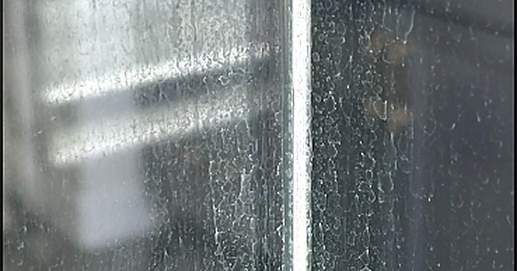 Vidrio de cancel de baño cubierto de manchas blancas de sarro por agua dura